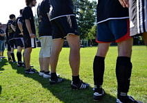 6 Männer von hinten in kurzen Sportklamotten stehen auf einem Fußballplatz.
