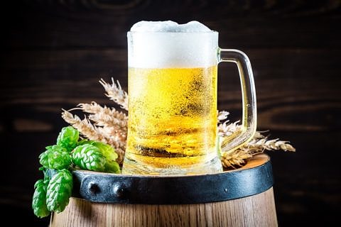 ein Glas Bier auf einem Fass, daneben liegen Hopfen und Gerste